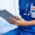 Cropped image of female doctor wearing scrubs reading a digital tablet